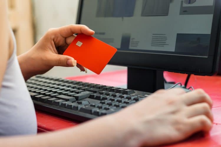 close-up of a hand clutching a credit card, looking at the website to purchase